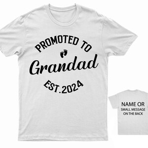 May include: White t-shirt with black text that reads "Promoted to Grandad Est. 2024" with a pair of baby footprints above the word "Grandad".