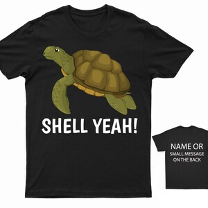 May include: Black t-shirt featuring a cartoon green sea turtle and the text "Shell Yeah!" printed in white. The back of the shirt is blank.