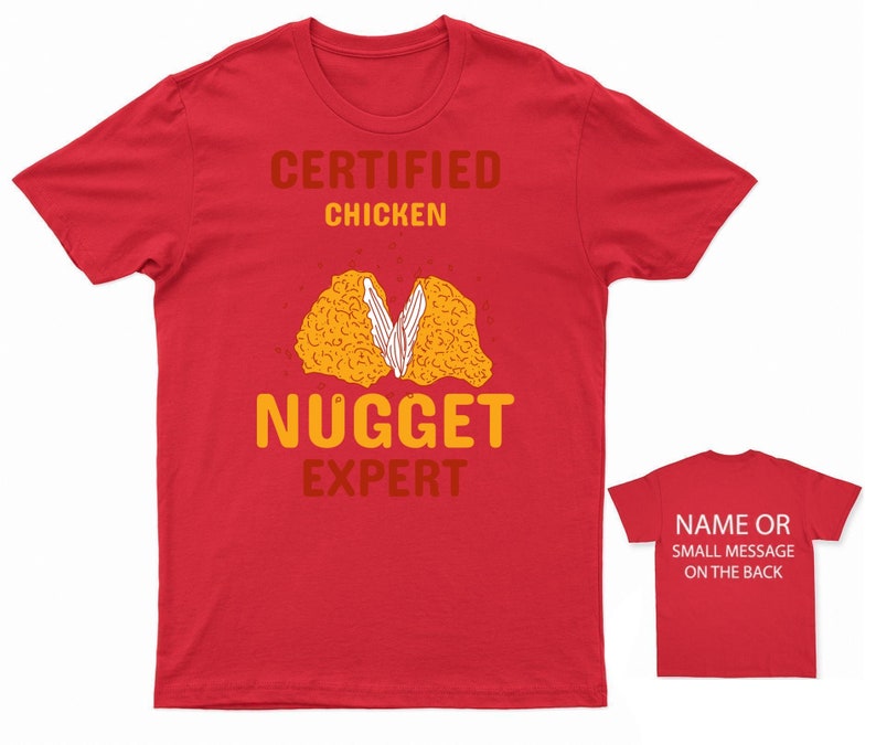 Op de afbeelding: Rood T-shirt met de tekst "Certified Chicken Nugget Expert" en een cartoon afbeelding van een kipnugget. De achterkant van het shirt heeft ruimte voor een naam of een klein bericht.