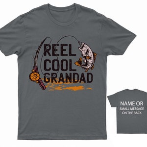 May include: Dark gray t-shirt with a fishing rod and fish graphic. The text "Reel Cool Grandad" is printed on the shirt.
