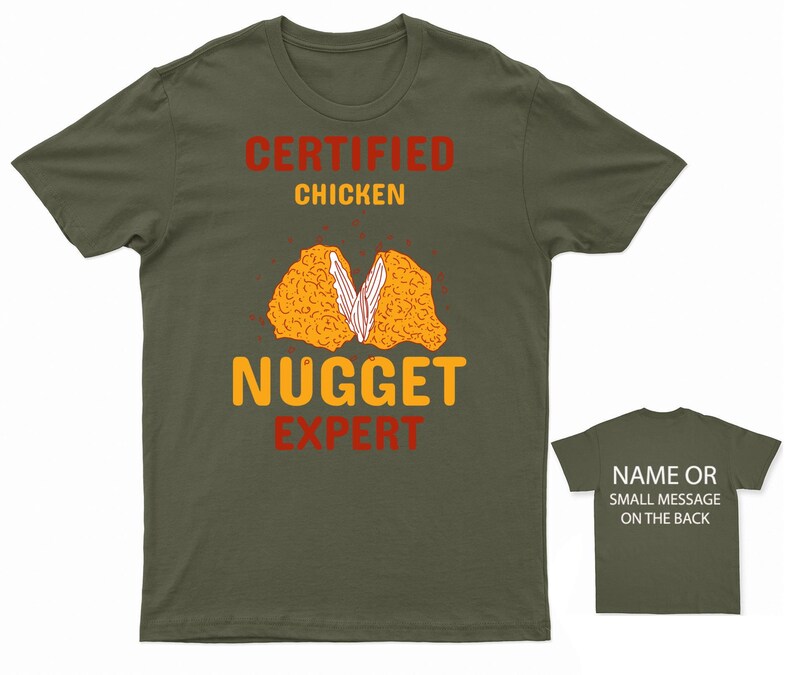 Op de afbeelding: Een groen T-shirt met de tekst "Certified Chicken Nugget Expert" in rood en geel. Het shirt heeft een afbeelding van een gehalveerd kippennugget.