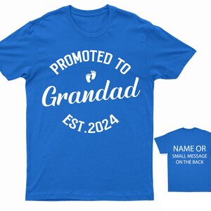 May include: Blue t-shirt with white text that reads "Promoted to Grandad Est. 2024" with a pair of baby footprints above the word "Grandad".
