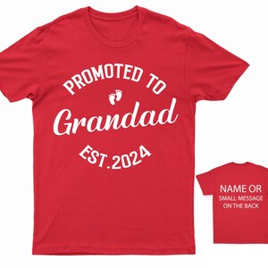 May include: Red t-shirt with white text that reads "Promoted to Grandad Est. 2024" with a pair of baby footprints above the word "Grandad".