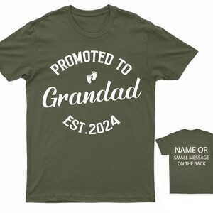 May include: Olive green t-shirt with white text that reads "Promoted to Grandad Est. 2024" with two small footprints above the word "Grandad".