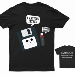 May include: Black t-shirt featuring a white graphic of a floppy disk and a USB drive. The floppy disk has a face and says "I am your father". The USB drive has a face and says "Noooo".