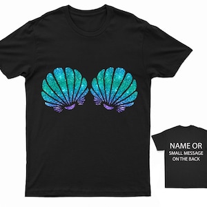 May include: Black t-shirt featuring a glittery turquoise and purple seashell design. The back of the shirt has the text "NAME OR SMALL MESSAGE ON THE BACK".