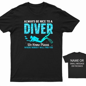 May include: Black t-shirt with a blue and white graphic of a scuba diver. The text "ALWAYS BE NICE TO A DIVER We Know Places WHERE NOBODY WILL FIND YOU" is printed on the shirt.
