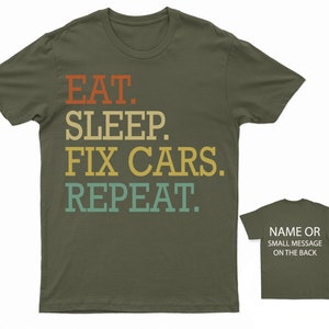 Puede incluir: Una camiseta verde con el texto "EAT. SLEEP. FIX CARS. REPEAT." en un esquema de color retro. La parte posterior de la camiseta est&aacute; en blanco y se puede personalizar con un nombre o un mensaje.