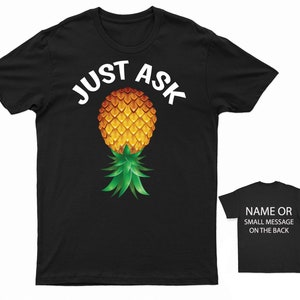 May include: Black t-shirt with the text "JUST ASK" in white letters and a pineapple graphic. The pineapple is yellow and green with a brown stem.