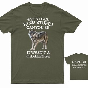 K&ouml;nnte beinhalten: Ein gr&uuml;nes T-Shirt mit einer wei&szlig;en Wolfgrafik und dem Text "WHEN I SAID HOW STUPID CAN YOU BE IT WASN'T A CHALLENGE". Auf der R&uuml;ckseite des Shirts steht "NAME OR SMALL MESSAGE ON THE BACK".