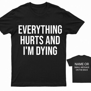 May include: Black t-shirt with white text that reads "Everything Hurts and I'm Dying". A smaller black t-shirt is shown in the background with white text that reads "Name or Small Message on the Back".