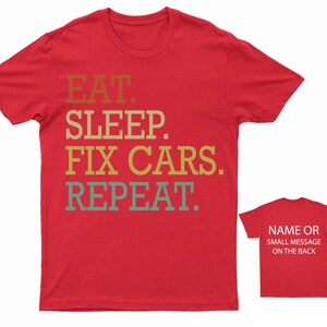 Puede incluir: Camiseta roja con el texto "EAT. SLEEP. FIX CARS. REPEAT." en una fuente retro. La parte posterior de la camiseta tiene espacio para un nombre o un mensaje peque&ntilde;o.
