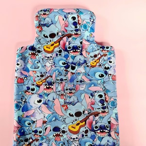 May include: Blue and white fabric with a repeating pattern of Stitch characters from the Disney movie Lilo & Stitch. The characters are playing ukuleles and some are wearing leis.