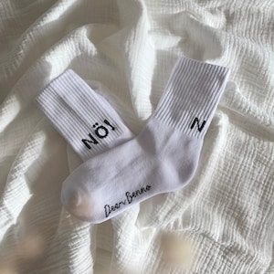 Könnte beinhalten: Ein Paar weiße Socken mit schwarzer Beschriftung. Eine Socke sagt "NO!" und die andere sagt "N". Die Socken tragen den Schriftzug "Deari Benno".