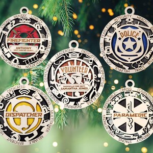 Könnte beinhalten: Fünf hölzerne Weihnachtsschmuckstücke, die jeweils einen anderen Beruf darstellen: Feuerwehrmann, Polizist, Freiwilliger, Disponent und Sanitäter. Die kreisförmigen Ornamente zeigen berufsbezogene Symbole und Texte, einschließlich Namen und Abteilungsdetails.