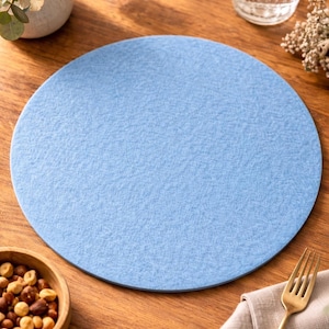 Könnte beinhalten: Ein runder, hellblauer Filz-Tischset liegt auf einem Holztisch. Eine goldene Gabel liegt auf einer beigen Serviette. Eine kleine Holzschale mit Nüssen und ein Glas Wasser mit Zitrone sind ebenfalls zu sehen.