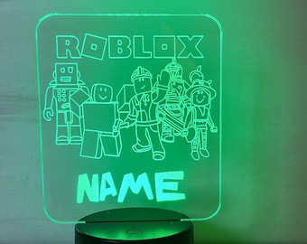 May include: A green illuminated acrylic sign with the word "ROBLOX" and a group of cartoon characters. The sign also includes the word "NAME" at the bottom.