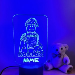 May include: A blue and white 3D printed night light featuring a Roblox character with the text "Roblox Name".