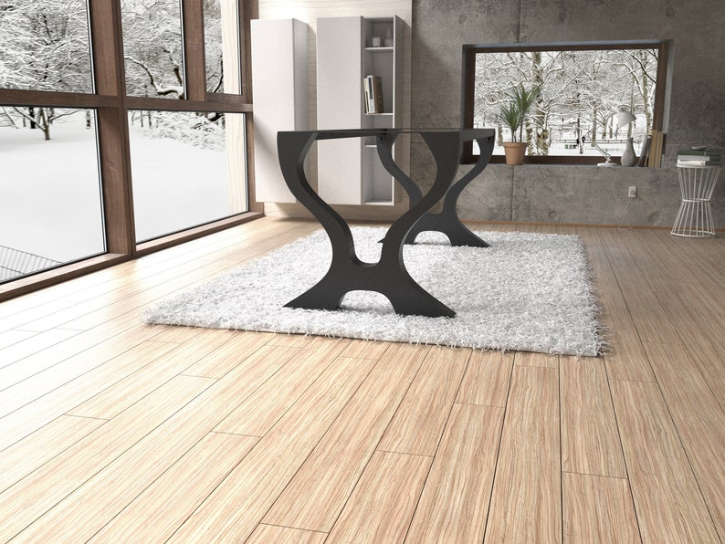 May include: Black metal table base with a unique, curved design. The base is sitting on a white rug in a room with wooden floors.