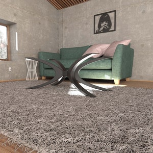 Puede incluir: Una alfombra de pelo gris con una mesa de caf&eacute; de metal negro delante de un sof&aacute; de color turquesa con almohadas rosas. El sof&aacute; est&aacute; en una habitaci&oacute;n con una pared de hormig&oacute;n y una foto en blanco y negro enmarcada.