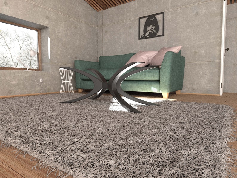 Puede incluir: Una alfombra de pelo gris con una mesa de caf&eacute; de metal negro delante de un sof&aacute; de color turquesa con almohadas rosas. El sof&aacute; est&aacute; en una habitaci&oacute;n con una pared de hormig&oacute;n y una foto en blanco y negro enmarcada.