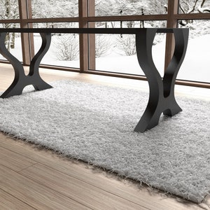 May include: A black, modern dining table with a rectangular glass top and two unique, curved, black metal legs. The table is sitting on a white shag rug.