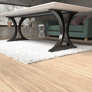 May include: A dining table featuring a thick, rectangular white tabletop supported by two black, curved metal legs. The base of each leg forms an arch shape that connects to the floor, providing a stable foundation for the flat, smooth surface.