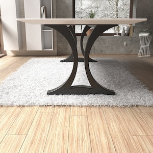 May include: A dining table featuring a flat, rectangular white top supported by two black metal bases. Each base consists of two curved, arching supports that meet in the center, creating a symmetrical silhouette that rests on a flat floor.