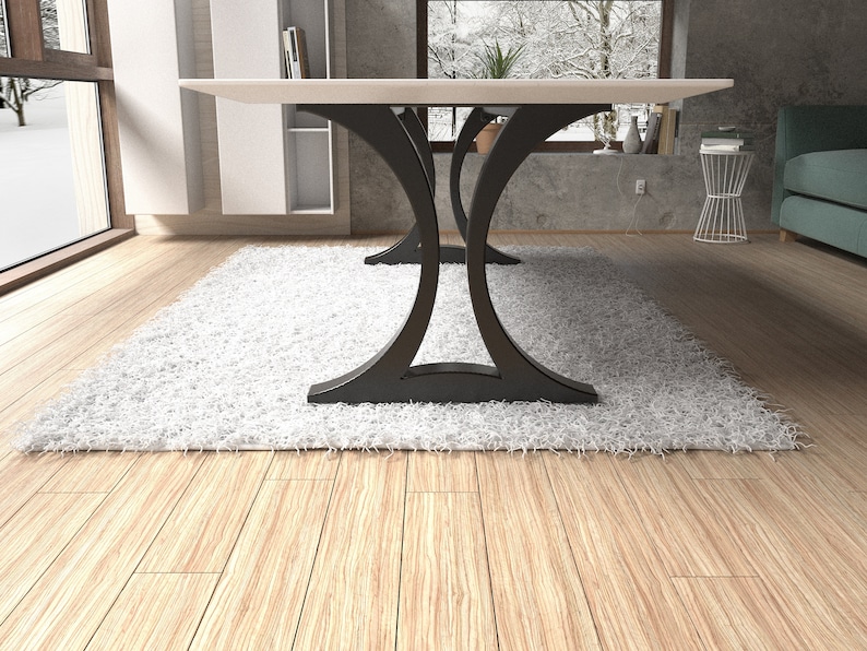 May include: A dining table featuring a flat, rectangular white top supported by two black metal bases. Each base consists of two curved, arching supports that meet in the center, creating a symmetrical silhouette that rests on a flat floor.