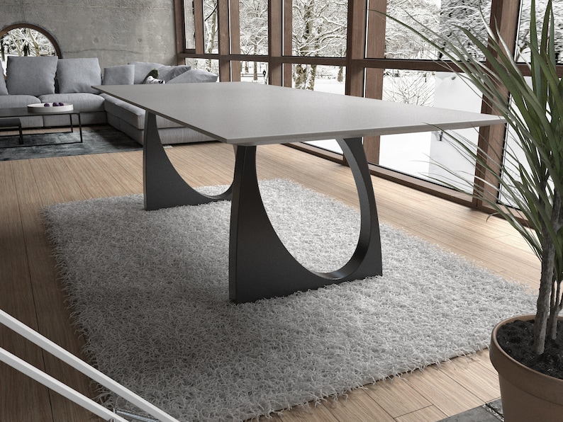 May include: A modern dining table with a gray concrete top and black metal legs. The legs are shaped like a crescent moon and are attached to the underside of the table top.