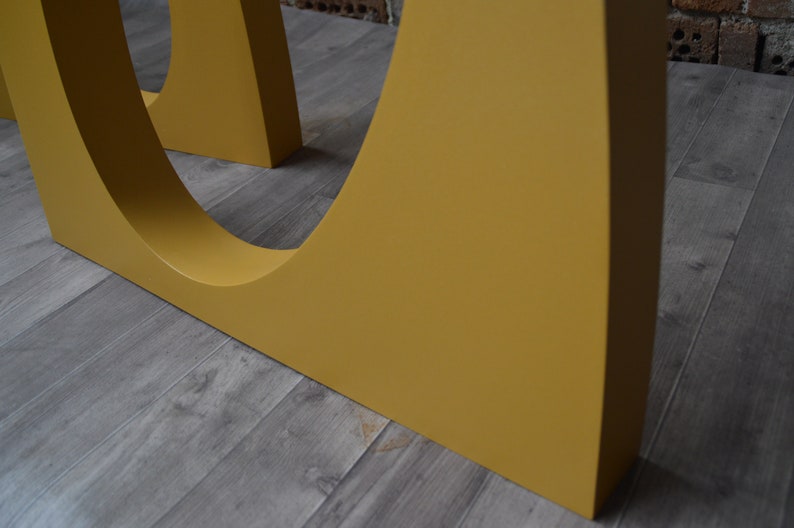May include: Close-up of a yellow table leg with a curved design. The leg is made of wood and has a smooth finish.
