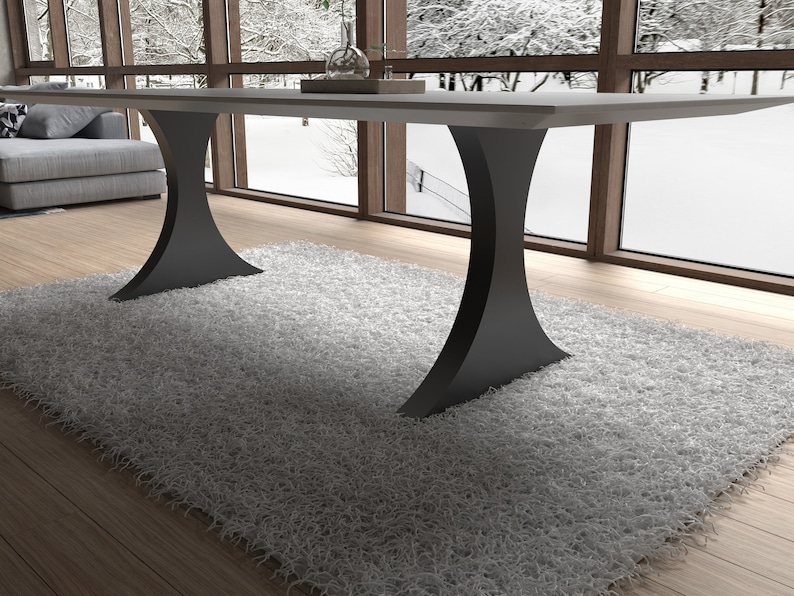 May include: A modern dining table with a white top and two black, curved legs. The table is set on a gray rug in a room with large windows.