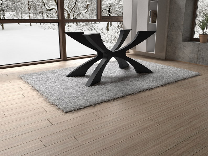 May include: A modern, black table base with a unique, geometric design. The base is made of metal and has multiple curved legs that intersect at the center. It sits on a gray, shaggy rug, with a snowy outdoor scene visible through a large window.