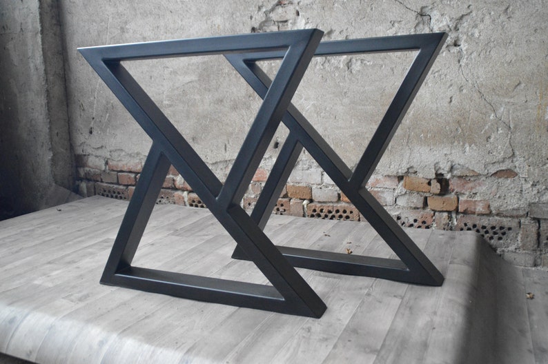 May include: Two black metal table legs with a geometric, triangular design. The legs are made of thick, sturdy metal and have a matte black finish.