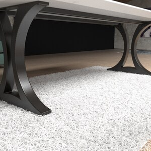 May include: A table with a smooth white rectangular top supported by two black metal legs. Each leg features a curved, arch-like design that flares outward at the base and top, providing a stable foundation for the tabletop surface above.