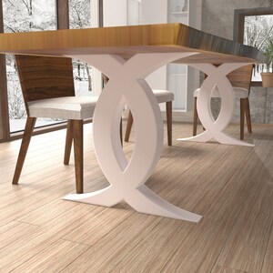 Puede incluir: Una mesa de comedor de madera con una base blanca en forma de doble X. La mesa se muestra con dos sillas, una con un coj&iacute;n blanco y la otra con un coj&iacute;n marr&oacute;n.
