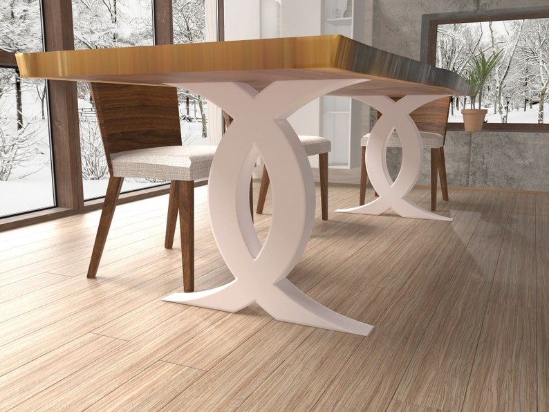 Puede incluir: Una mesa de comedor de madera con una base blanca en forma de doble X. La mesa se muestra con dos sillas, una con un coj&iacute;n blanco y la otra con un coj&iacute;n marr&oacute;n.