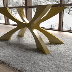 May include: A modern table base with a unique design. The base is made of a light yellow material and features an intricate, starburst-like structure. The table is set on a fluffy, white rug in front of a large window.