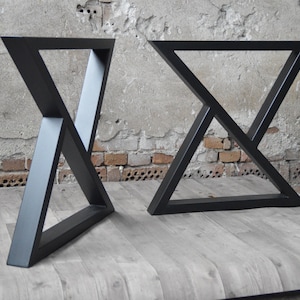 May include: Two black metal table legs with a triangular design. The legs are made of thick metal and have a matte black finish.