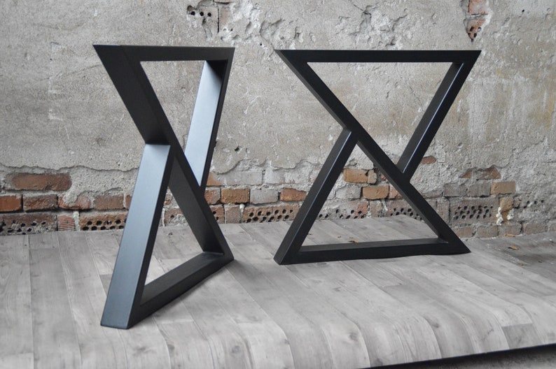 May include: Two black metal table legs with a triangular design. The legs are made of thick metal and have a matte black finish.