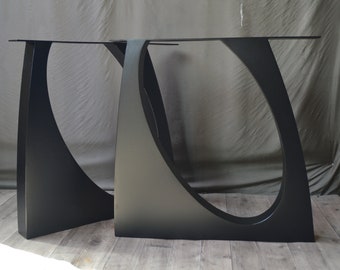 May include: Two black metal table legs with a curved, abstract design. The legs are made of thick, sturdy metal and have a matte black finish.