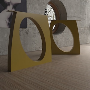 May include: Two gold metal side tables with oval cutouts. The tables are in a room with a concrete wall and a window with a view of a snowy forest.