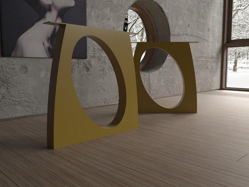 May include: Two gold metal side tables with oval cutouts. The tables are in a room with a concrete wall and a window with a view of a snowy forest.