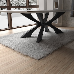 May include: A modern dining table with a light-colored rectangular top and a unique black base. The base features a series of curved, intersecting supports. The table sits on a fluffy, light gray rug, with a wooden floor beneath.