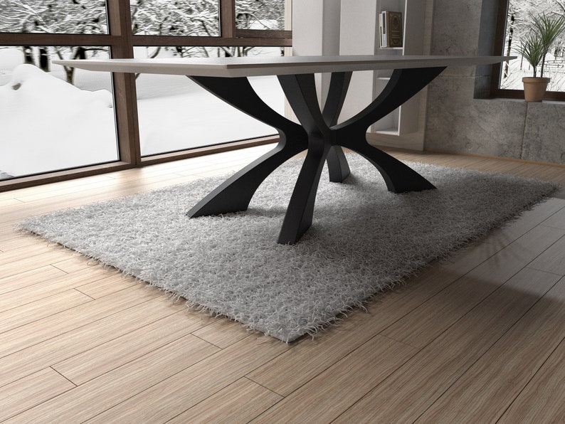 May include: A modern dining table with a light-colored rectangular top and a unique black base. The base features a series of curved, intersecting supports. The table sits on a fluffy, light gray rug, with a wooden floor beneath.