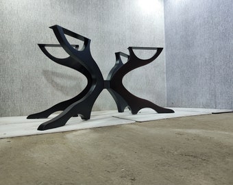 May include: Black metal table base with a unique, abstract design. The base has four legs that curve and connect in the center, creating a symmetrical X shape.