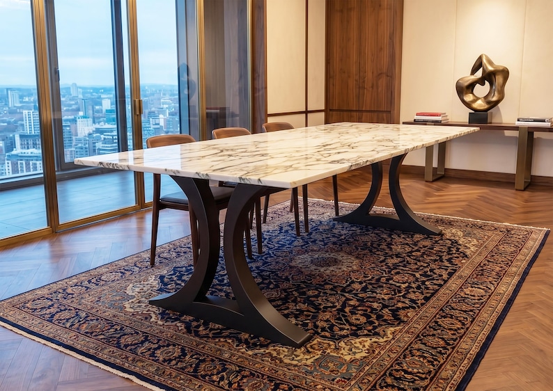 May include: A rectangular dining table featuring a polished white marble top with prominent grey veining. The table is supported by two curved, matte black metal pedestal bases that flare outward at the floor and the tabletop connection points.