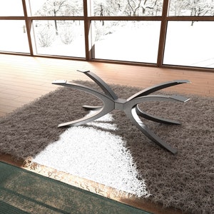 Puede incluir: Una base de mesa de metal plateado con un dise&ntilde;o curvo &uacute;nico. La base est&aacute; sentada sobre una alfombra de pelo marr&oacute;n y blanco.