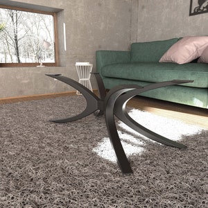 Puede incluir: Una mesa de centro de metal negro con una base &uacute;nica en forma de X curvada. La mesa est&aacute; sobre una alfombra de pelo gris en un sal&oacute;n.