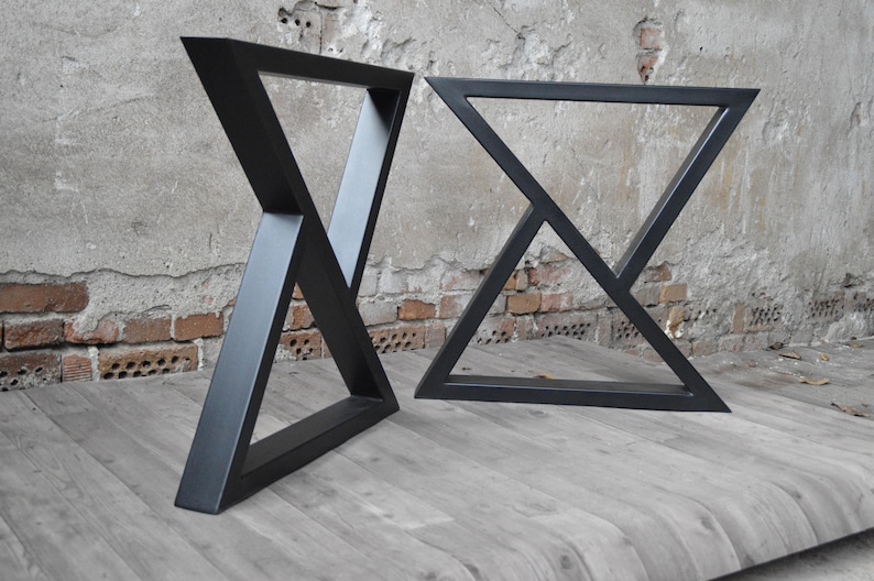 May include: Two black metal table legs with a triangular design. The legs are made of thick metal and have a matte black finish.